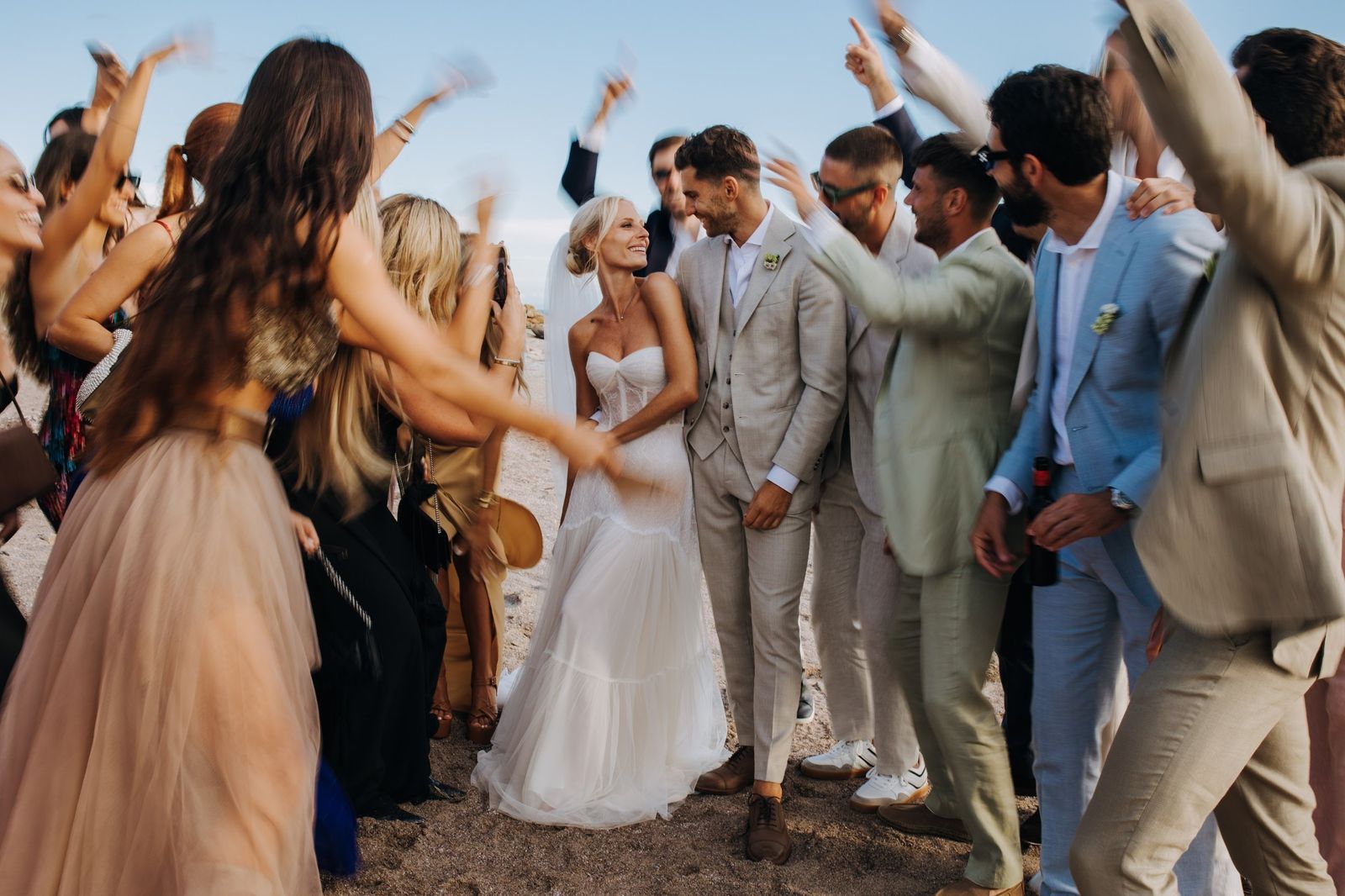 Novios mirándose en la playa mientras sus amigos celebran a su alrededor